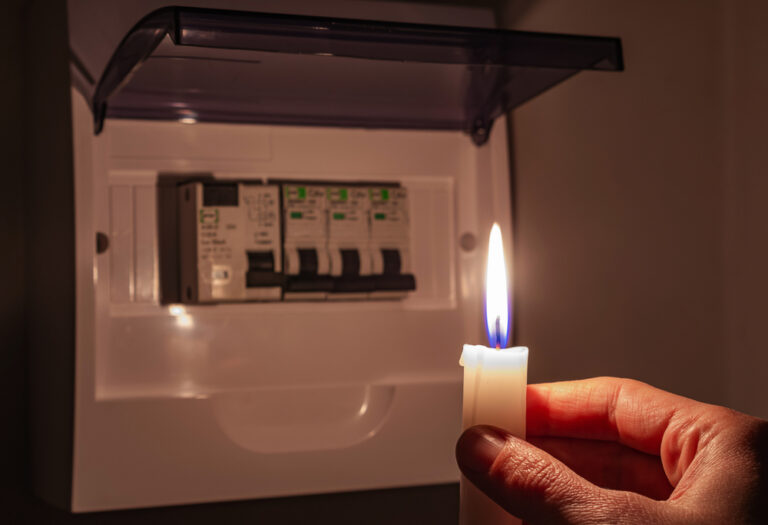 Woman in total darkness holding a candle checking fuse box at home during a power outage.