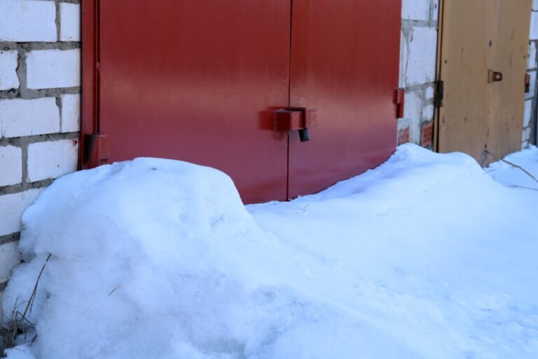 Background of white snow on a red corrugated fence and asphalt, soft focus - Protecting Your Garage Door During Hurricane Season: Expert Advice