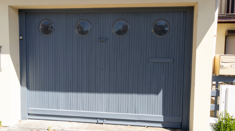 Custom grey wooden overlay garage door featuring round windows, installed on a residential house.